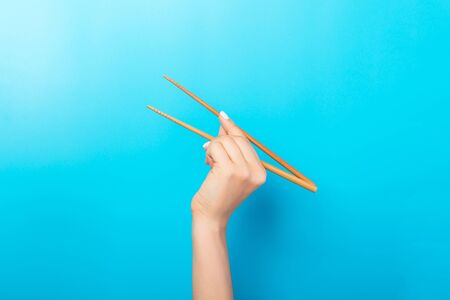 Female hand with chopsticks on blue background. Traditional asian food with emty space for your design.の写真素材
