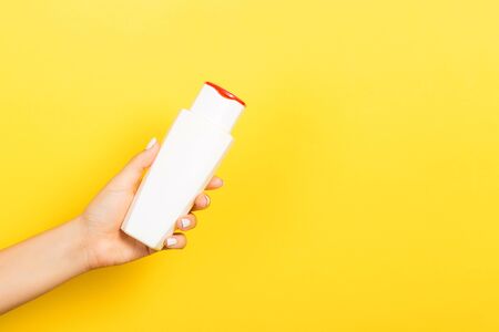 Female hand holding cream bottle of lotion isolated. Girl give tube cosmetic products on yellow background.の写真素材