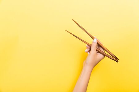 Female hand with chopsticks on yellow background. Traditional asian food with emty space for your design.の写真素材