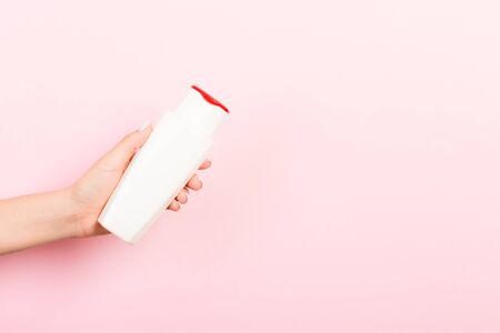 Female hand holding cream bottle of lotion isolated. Girl give tube cosmetic products on pink...