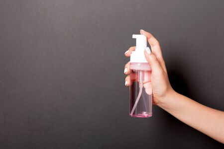 Female hand holding spray cream bottle of lotion isolated. Girl give cosmetic products on black background.の写真素材