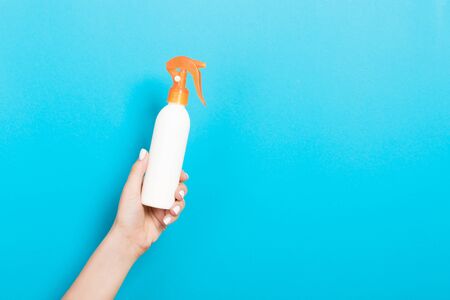 Female hand holding spray cream bottle of lotion isolated. Girl give cosmetic products on blue background.の写真素材