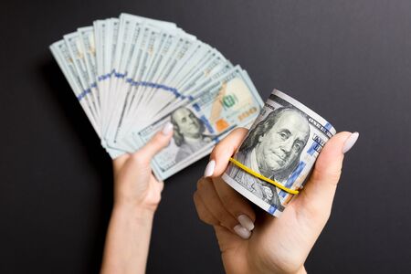 Top view of female hand holding a fan of money on colorful background. One hundred dollar bills....