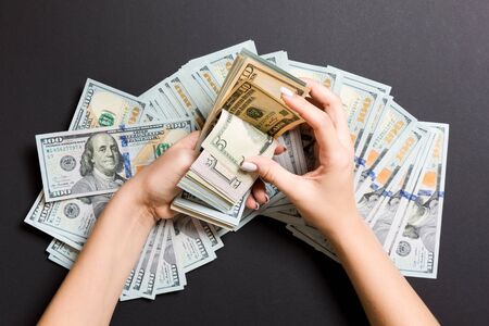 Businesswoman's hands counting one hundred, five and other dollar bills on colorful background. Salary and wage concept. Top view of Investment concept.の写真素材