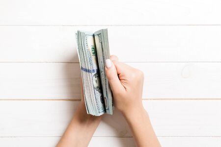 Top view of female hands counting money. One hundred dollar banknotes on wooden background. Salary...