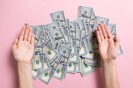Female hands lying on stack of one hundred dollar bills on colorful background. Saving money and wellbeing concept.の写真素材