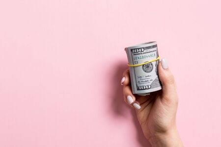 Top view of female hand holding a pack of rolled money on colorful background. One hundred dollars. Business concept with empty space for your design. Charity and tips concept.の写真素材