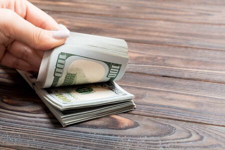 Perspective view of a businesswoman's hands counting one hundred dollar banknotes on wooden...