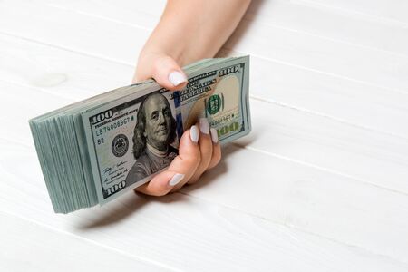 Perspective view of female hand giving one hundred dollar bills on wooden background. Charity and donation concept with copy space.の写真素材