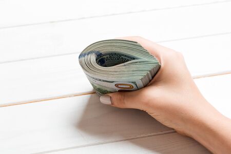 Perspective view of female hand holding a pack of money on wooden background. One hundred dollars....