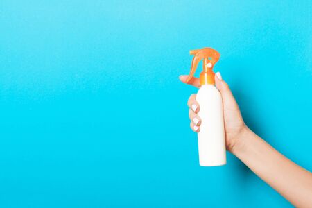 Female hand holding spray cream bottle of lotion isolated. Girl give cosmetic products on blue...