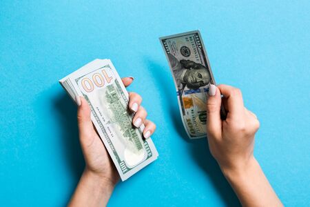 Female hand giving one hundred dollar banknotes on colorful background. Top view of wealth concept.の写真素材