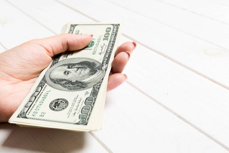 Female hand holding a bundle of money on wooden background. Perspective view of one hundred dollar...