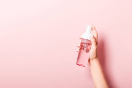 Female hand holding spray cream bottle of lotion isolated. Girl give cosmetic products on pink background.の写真素材