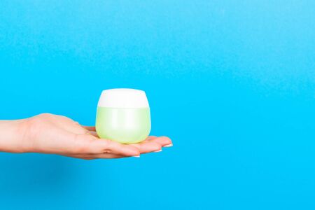 Female hand holding cream bottle of lotion isolated. Girl give jar cosmetic products on blue background.の写真素材
