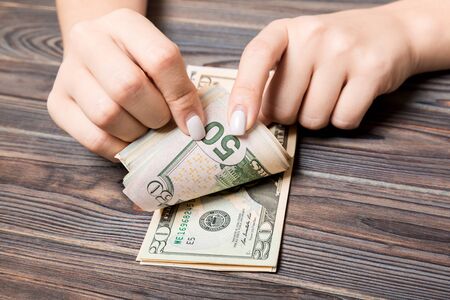 Perspective view of a businesswoman's hands counting fifty and twenty dollar banknotes on wooden background. Success and wealth concept.の写真素材