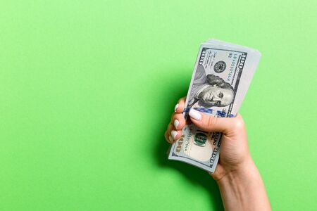 Female hand holding a bundle of one hundred dollar banknotes on colorful background. Salary and wage concept with copy space.の写真素材
