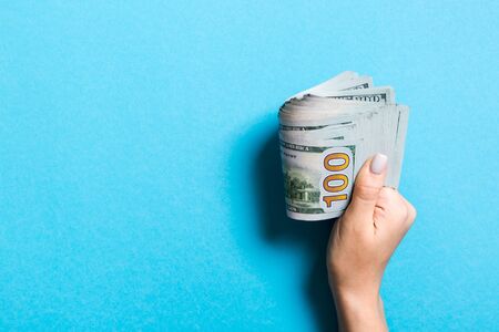 Female hand holding tightly a bundle of money. Top view of one hundred dollars on colorful background. Investment concept with copy space.の写真素材