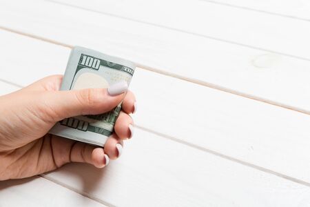 Perspective view of female hand holding a pack of money on wooden background. One hundred dollars....