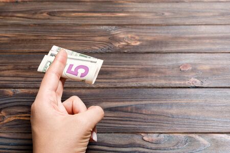 A pack of 5 dollar bills in female hand on wooden background. Salary concept with copy space.