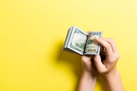 Businesswoman's hands counting one hundred dollar bills on colorful background. Salary and wage...