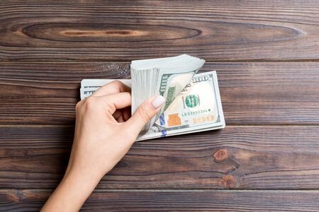 Top view of female hands counting money. One hundred dollar banknotes on colorful background....