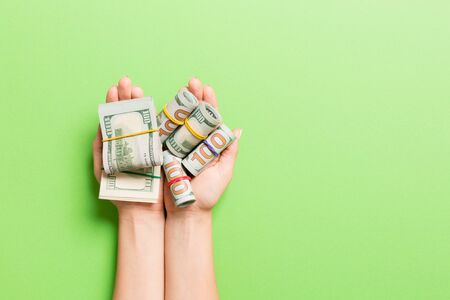 Top view of rolled up in tubes dollar bills in female palms on colorful background. Poverty and debt...