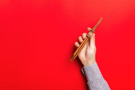 Cropped image of male hand holding chopsticks on red background. Asian food concept with copy space.の写真素材