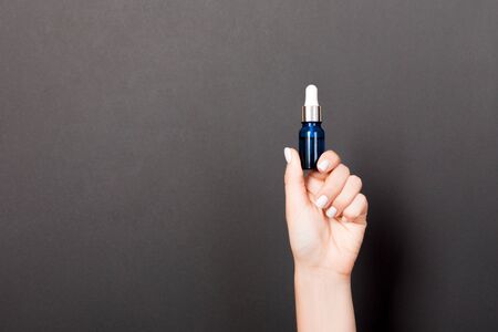 Female hand holding cream bottle of lotion isolated. Girl give tube cosmetic products on black background.の写真素材