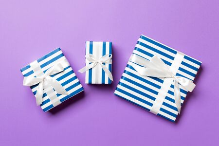 wrapped Christmas or other holiday handmade present in paper with White ribbon on purple background. Present box, decoration of gift on colored table, top view.の写真素材