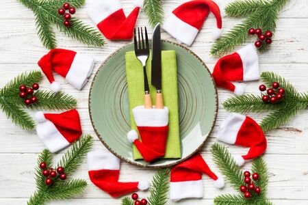 Holiday composition of plate and flatware decorated with Santa hat on wooden background. Top view of Christmas decorations. Festive time concept.の写真素材