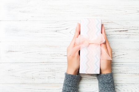 Female hands holding present on white rustic wooden background. Festive backdrop for Christmas...