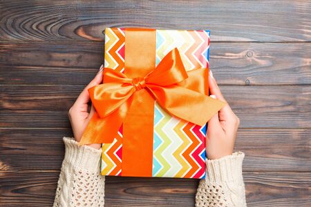 Female hands holding present on dark wooden background. Festive backdrop for Christmas holidays or...