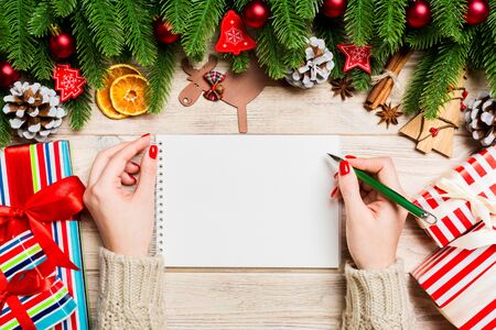 Top view of female hand writing in a notebook on wooden Christmas background. Fir tree and festive decorations. Wish list. New Year concept.の写真素材