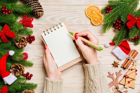 Top view of female hand writing in a notebook on wooden background with fir branches and festive decorations.の写真素材