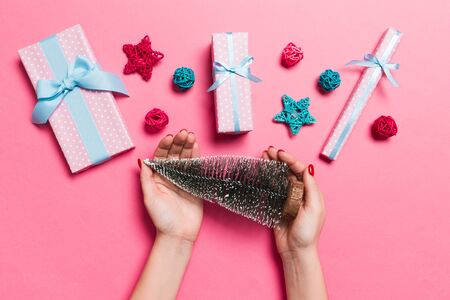 Top view of female hands holding christmas tree in her hand on pink background. New Year holiday concept. Mockup.の写真素材