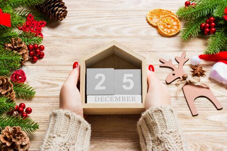 Top view of female hands holding a calendar on wooden background. The twenty fifth of December....