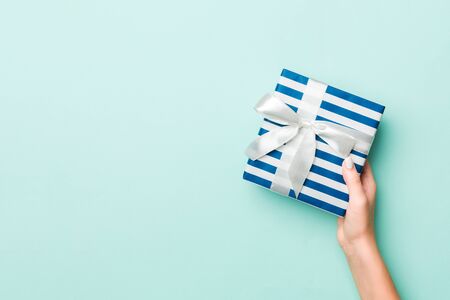 Woman hands give wrapped christmas or other holiday handmade present in colored paper. Present box,...