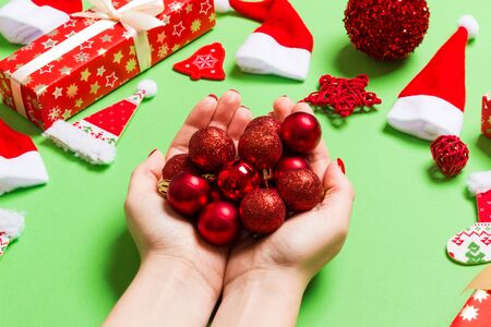 Top view of a heap of New Year balls in female hands on green backround made of festive decorations....