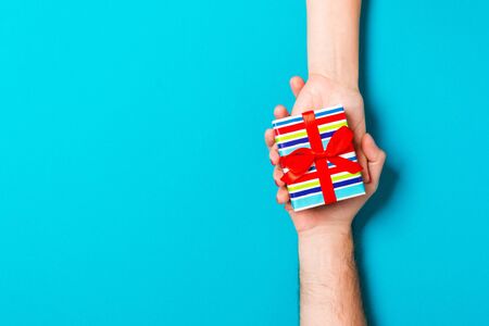 Top view of a gift in male and female hands on colorful background. Congratulation of each other concept. Copy space.の写真素材