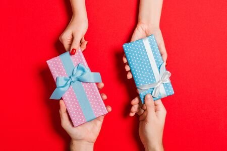 Top view of a woman and a man exchanging gifts on colorful background. Couple give presents to each other. Close up of making surprise for holiday concept.の写真素材