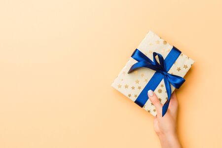 Flat lay of woman hands holding gift wrapped and decorated with bow on gold background with copy space. Christmas and holiday concept.の写真素材