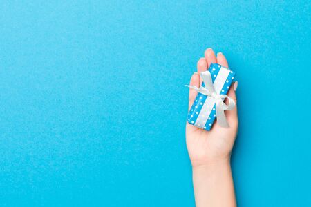 Woman arms holding gift box with colored ribbon on blue table background, top view and copy space for you design.の写真素材
