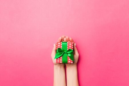 Girl Hands holding craft paper gift box with as a present for Christmas or other holiday on pink background, top view with copy sppace.の写真素材