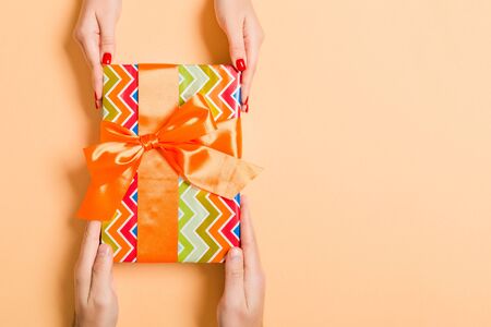 Top view of male and female hands holding present box on colorful background. Sharing a gift concept. Copy space.の写真素材
