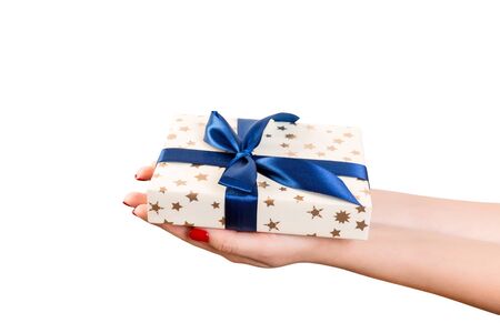 Woman hands give wrapped Christmas or other holiday handmade present in gold paper with blue ribbon. Isolated on white background, top view. thanksgiving Gift box concept.の写真素材