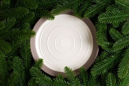 Top view of white plate surrounded with fir tree branches. Christmas dinner concept with copy space.の写真素材