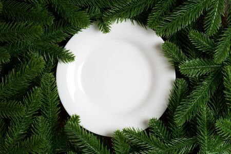 Top view of white plate surrounded with fir tree branches. Christmas dinner concept with copy space.の写真素材