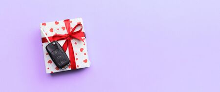Car key on paper gift box with red ribbon bow and heart on violet table background. Holidays present...