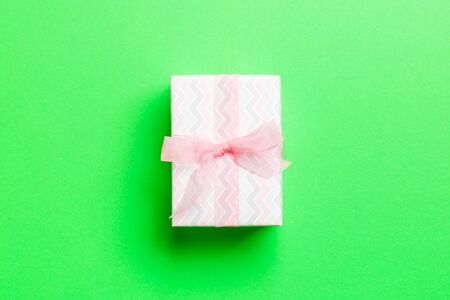 wrapped Christmas or other holiday handmade present in paper with pink ribbon on green background. Present box, decoration of gift on colored table, top view with copy space.の写真素材